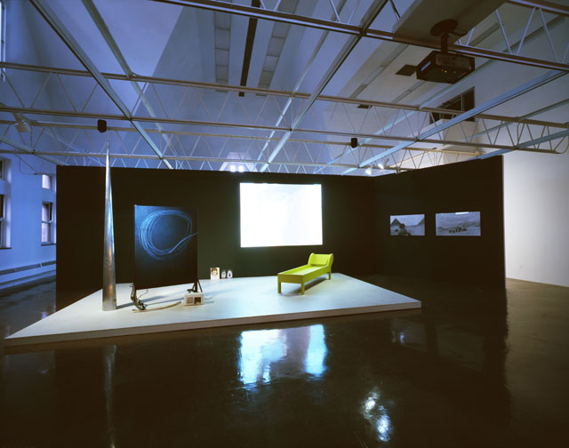 Joan Jonas. Lines in the Sand, 2002. Installation Video (Lines in the Sand 2002/2005. Colour, sound, 47:45 min), projection, blackboard, wooden structure, paint, video (Pillow Talk, 2002, colour, sound), monitor with performance video, green wooden couch, sand and relief box, plaster, photographs, paintings), dimensions variable. Museu d